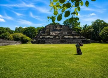 Tour card image of Altun Ha Maya ruins with a traveler on the grass in Belize.