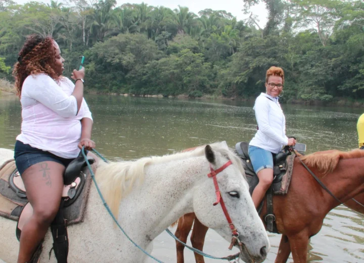 Guests horseback riding through a Belize river on a Xunantunich tour from Placencia