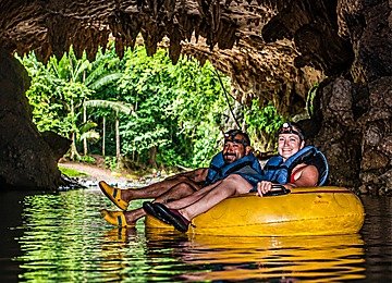 Couple enjoying Belize cave tubing in a yellow inner tube beneath dramatic cave formations and tropical jungle light.